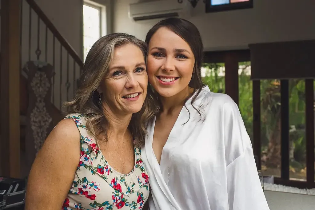 Bride and her mother smiling together while getting ready on the wedding morning